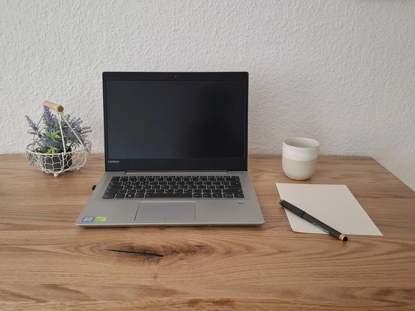 Arbeitsplatz für die Videositzungen: Laptop, Notizblock und Tasse auf einem Holztisch